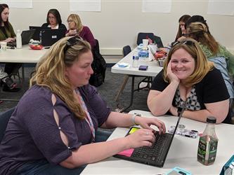 teachers working together in front of a laptop, one smiling at the camera