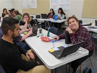 teachers working together on a table, one is smiling at the camera