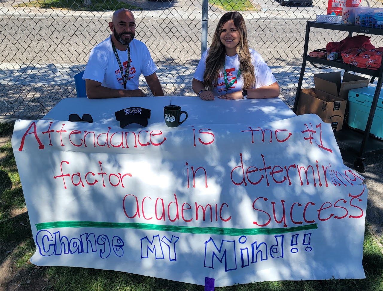 a man and woman sitting on a table with a written banner in front that says: 