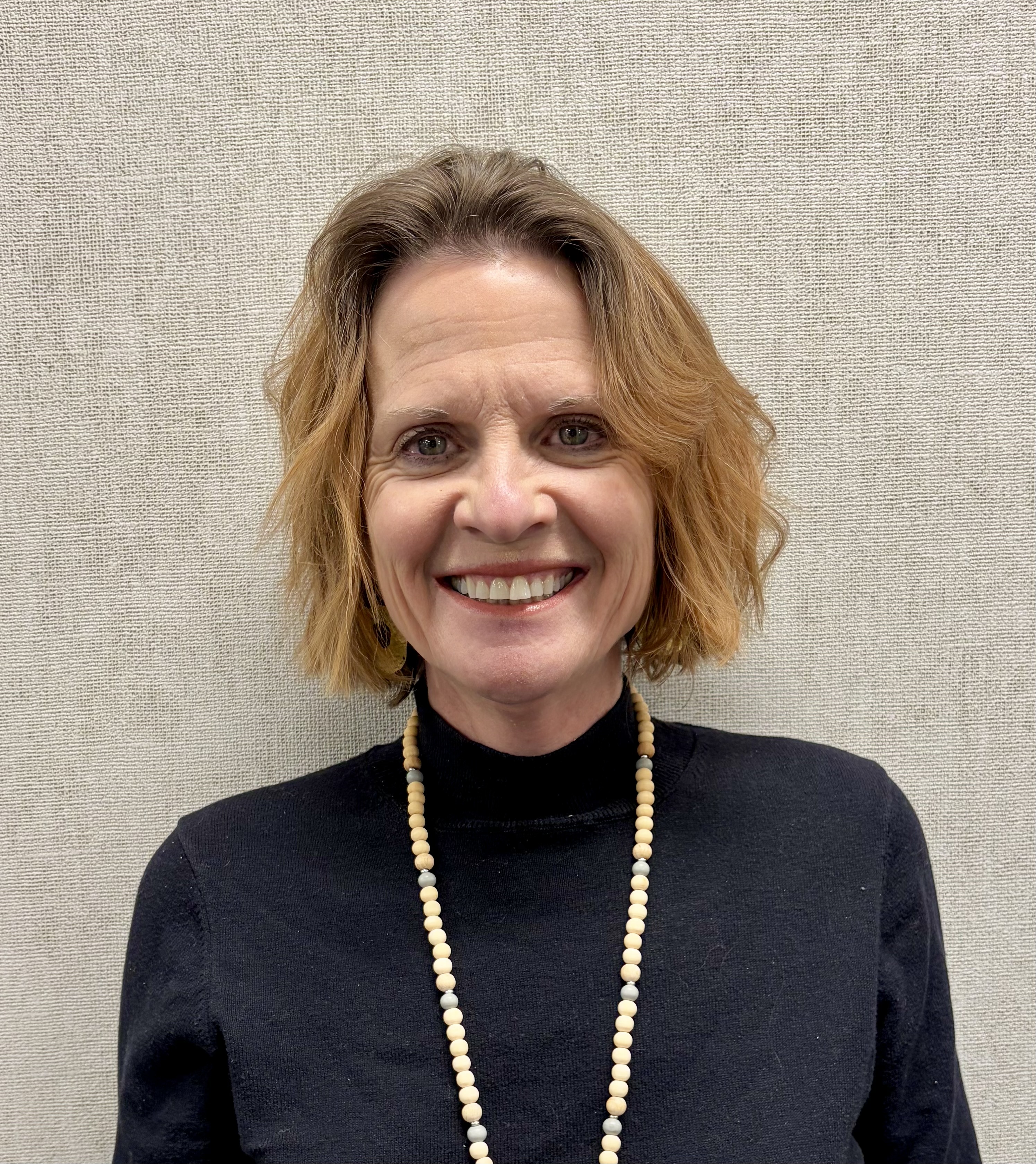 Smiling woman in a black shirt standing in front of a beige wall